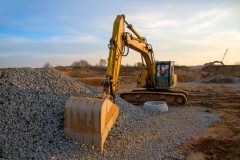 Excavator during earthmoving work at open-pit mining on blue sky background. Loader machine with bucket in sand quarry. Backhoe digging the ground for the foundation and for laying sewer pipes