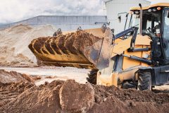 The excavator loader works with a bucket for transporting sand at a construction site. Professional construction equipment for earthworks