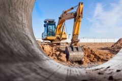 Heavy excavator at the construction site. View of the excavator through the iron pipe. Construction equipment for earthworks. Quarry excavator